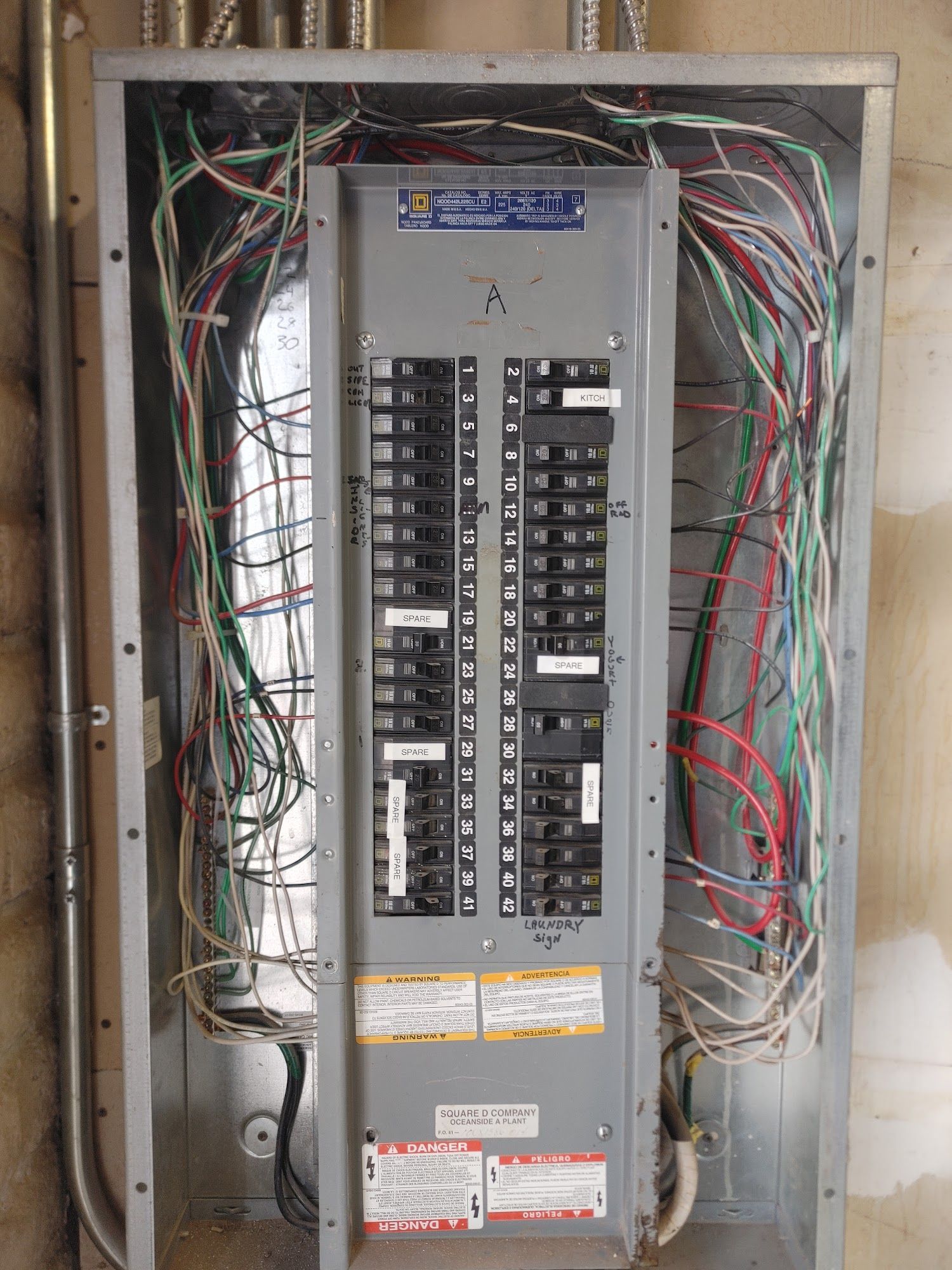 Electrical panel with numerous wires protruding from the sides, mounted in a metal box. Gray and silver hues dominate.