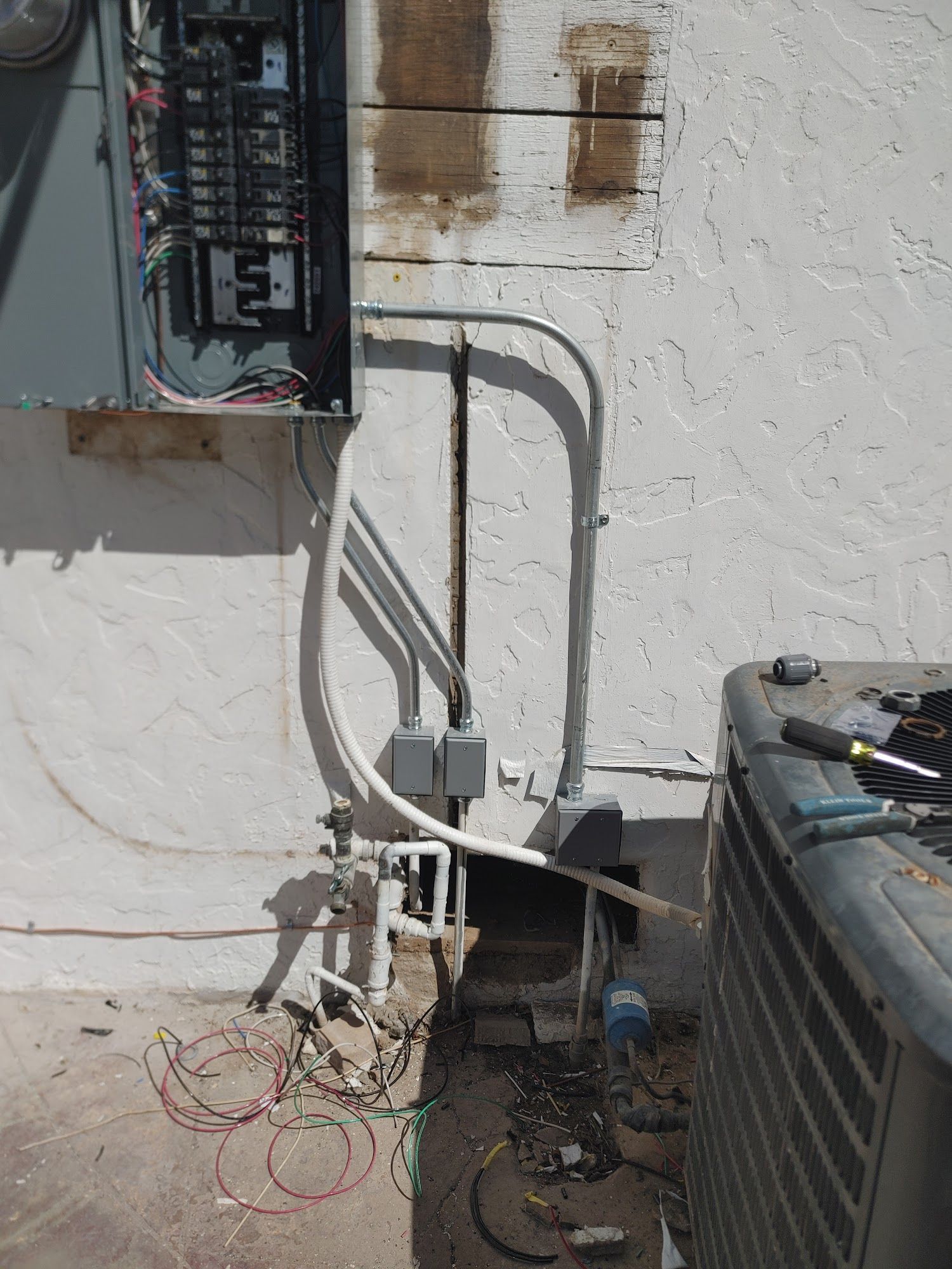 Electrical panel on stucco wall with conduit, wiring, and AC unit.