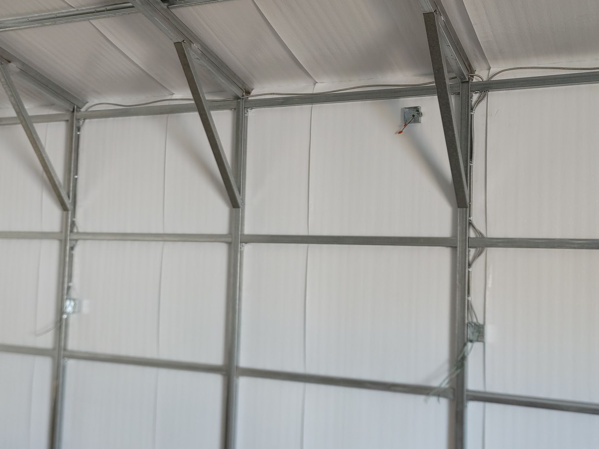 Interior view of a metal-framed building with white insulated walls and ceiling. Electrical boxes are visible.