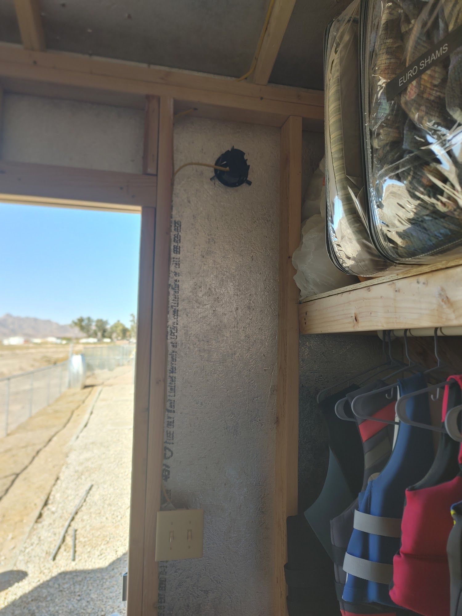 Inside shed: door, insulation, electrical fixture, shelf with bag, life vests hanging.