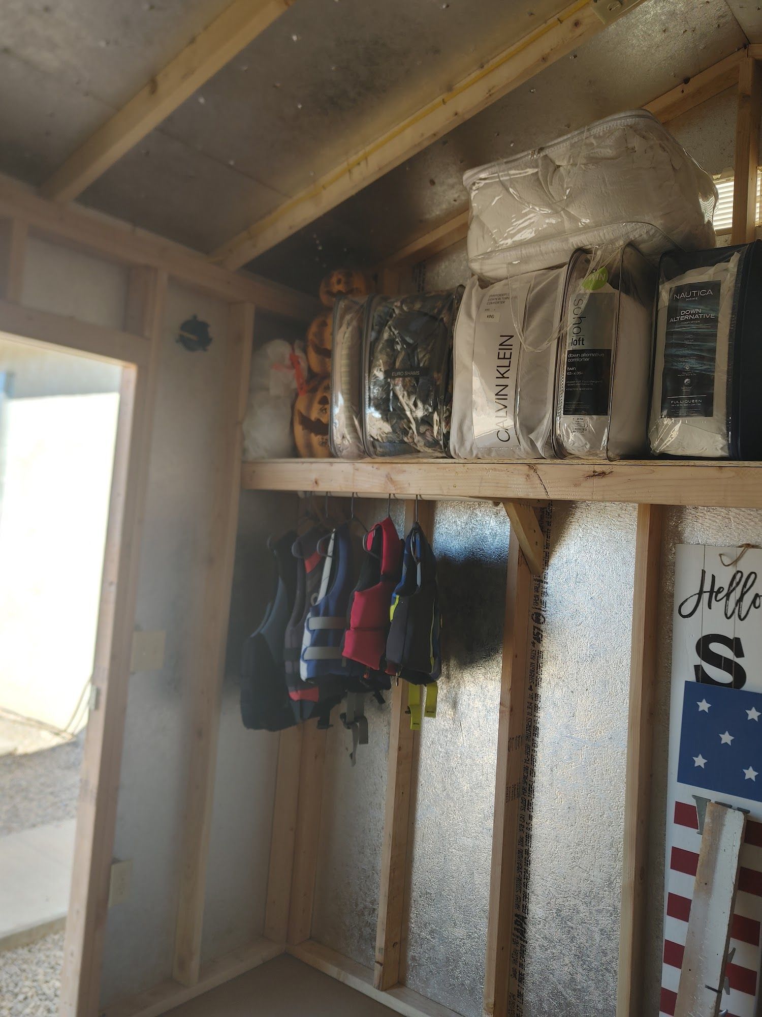 Inside a shed: shelves holding bags, jackets hanging below.  American flag art on the right.