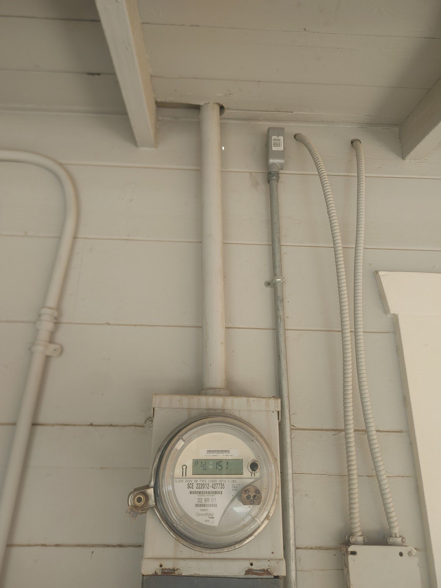 Electric meter on a gray wall with conduit and wiring.