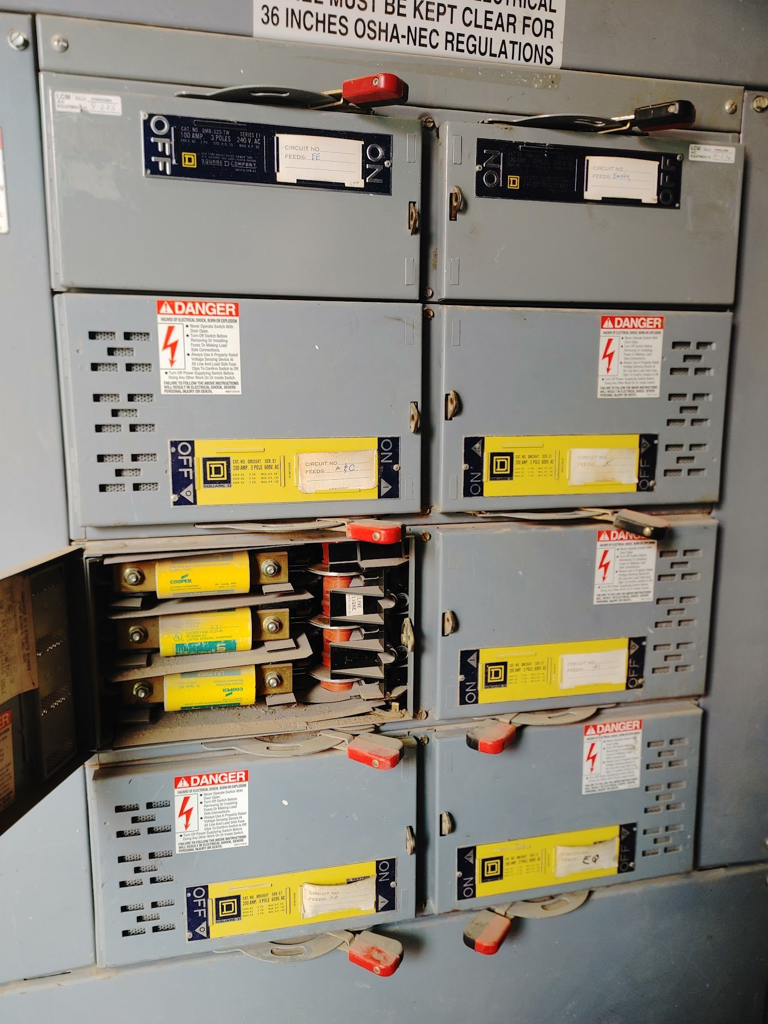 Electrical panel with several closed gray boxes and one open, revealing circuit breakers and wiring.