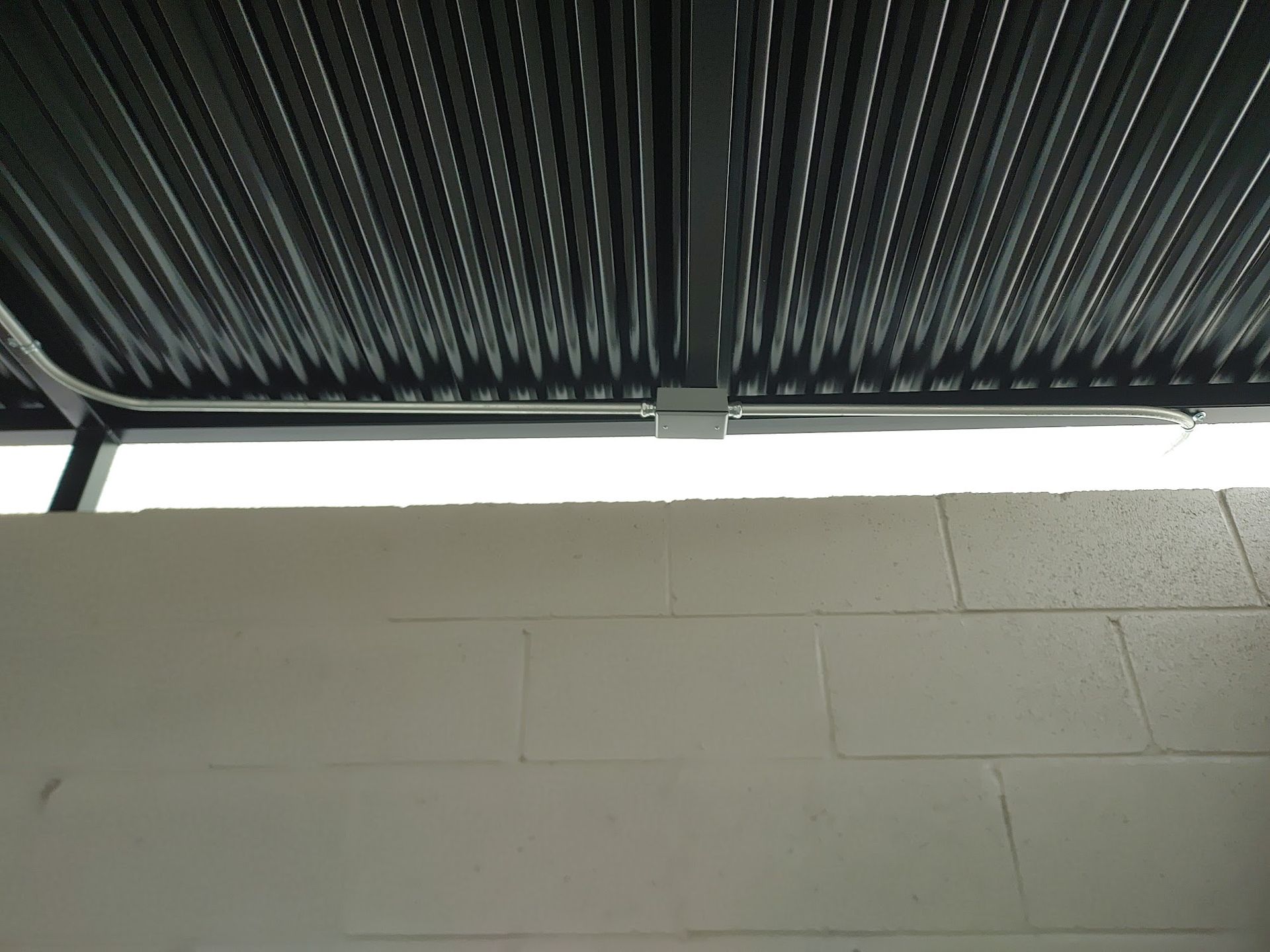 Gray corrugated ceiling above a white block wall, with a metal conduit and junction box.