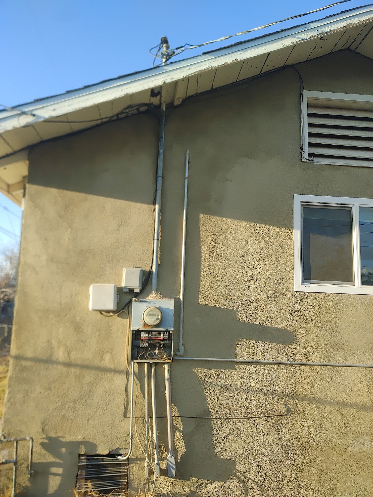 Exterior of a building with electrical meter box, conduit, and wires. Beige stucco wall, blue sky.