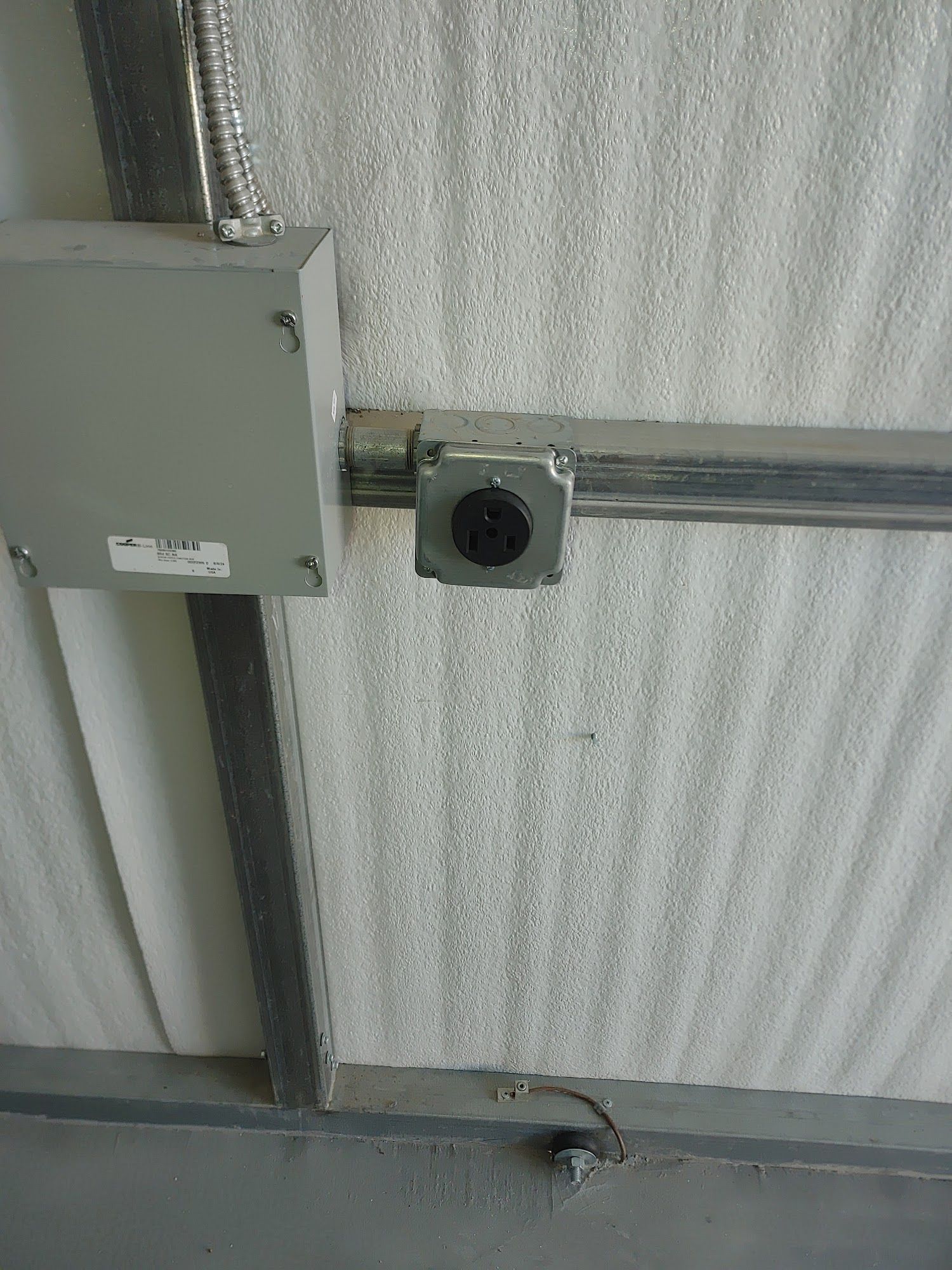Metal electrical outlet and junction box on a white, textured ceiling.