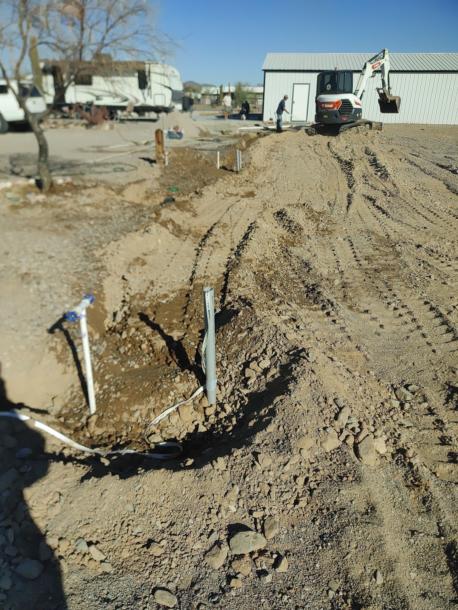 Dirt excavation with an excavator near a building and utility lines.