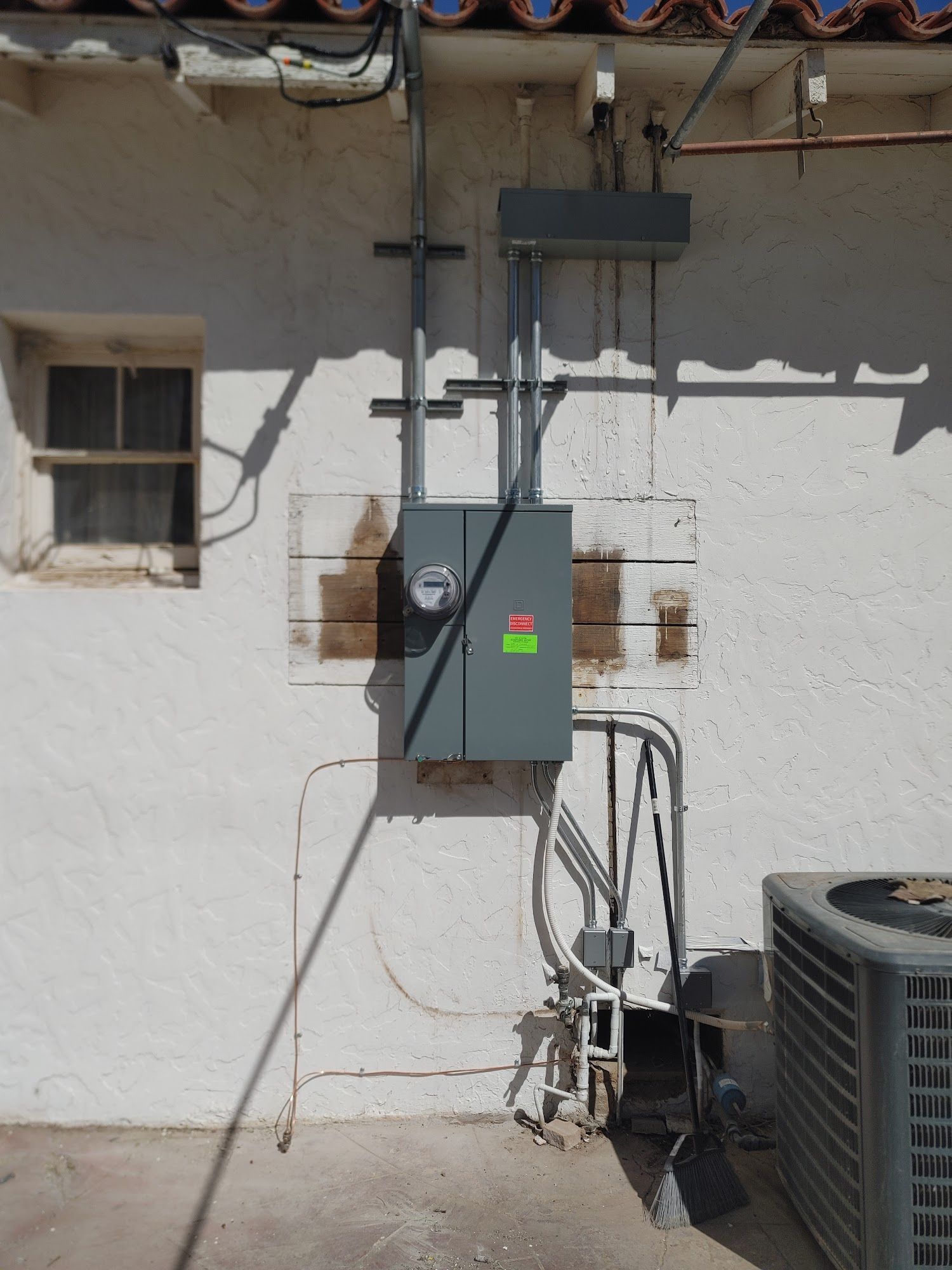 Exterior electrical panel mounted on a white stucco wall. Metallic conduit and wiring visible.