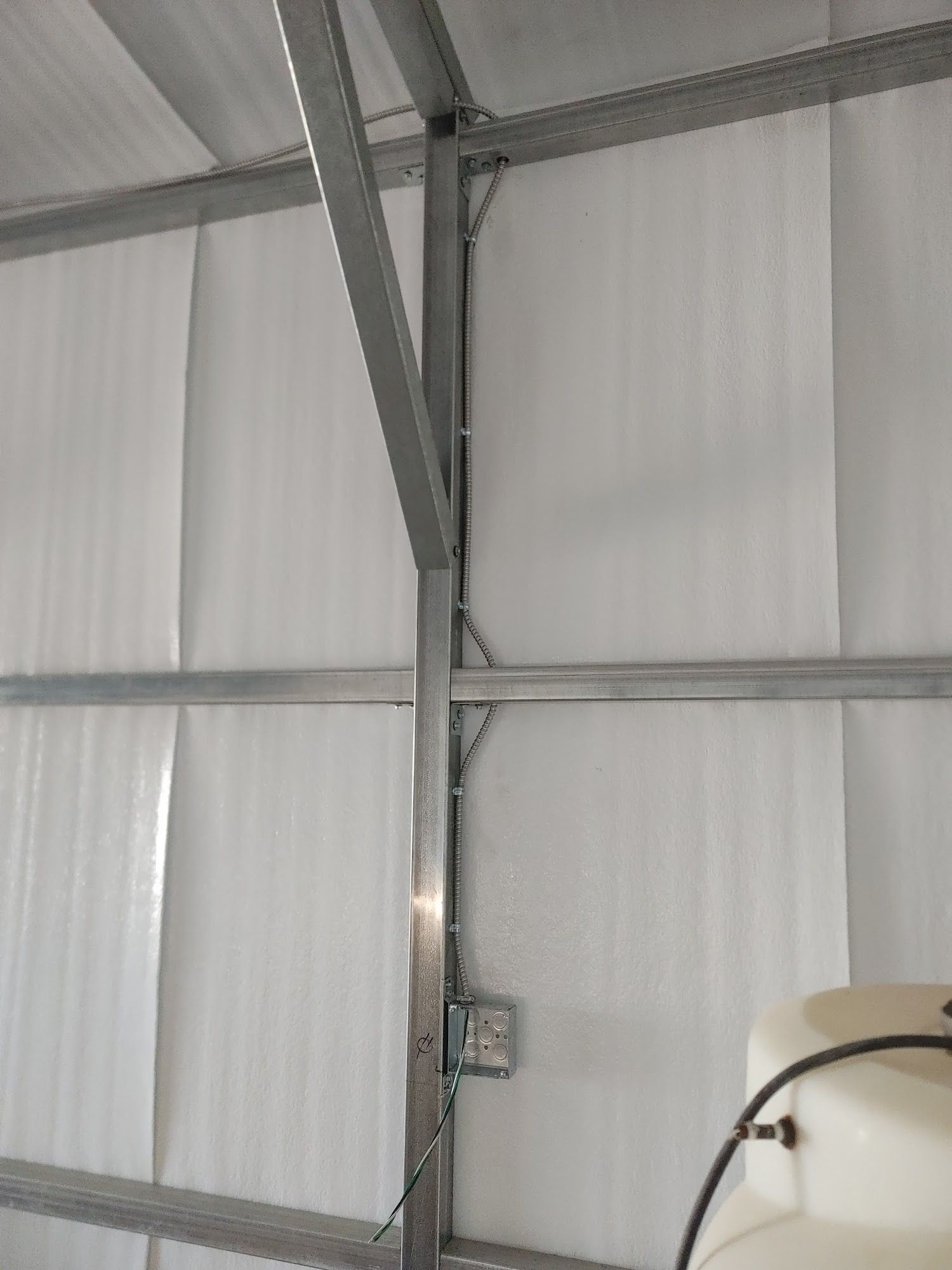 Interior view of a metal-framed building with white insulated walls and an electrical box.