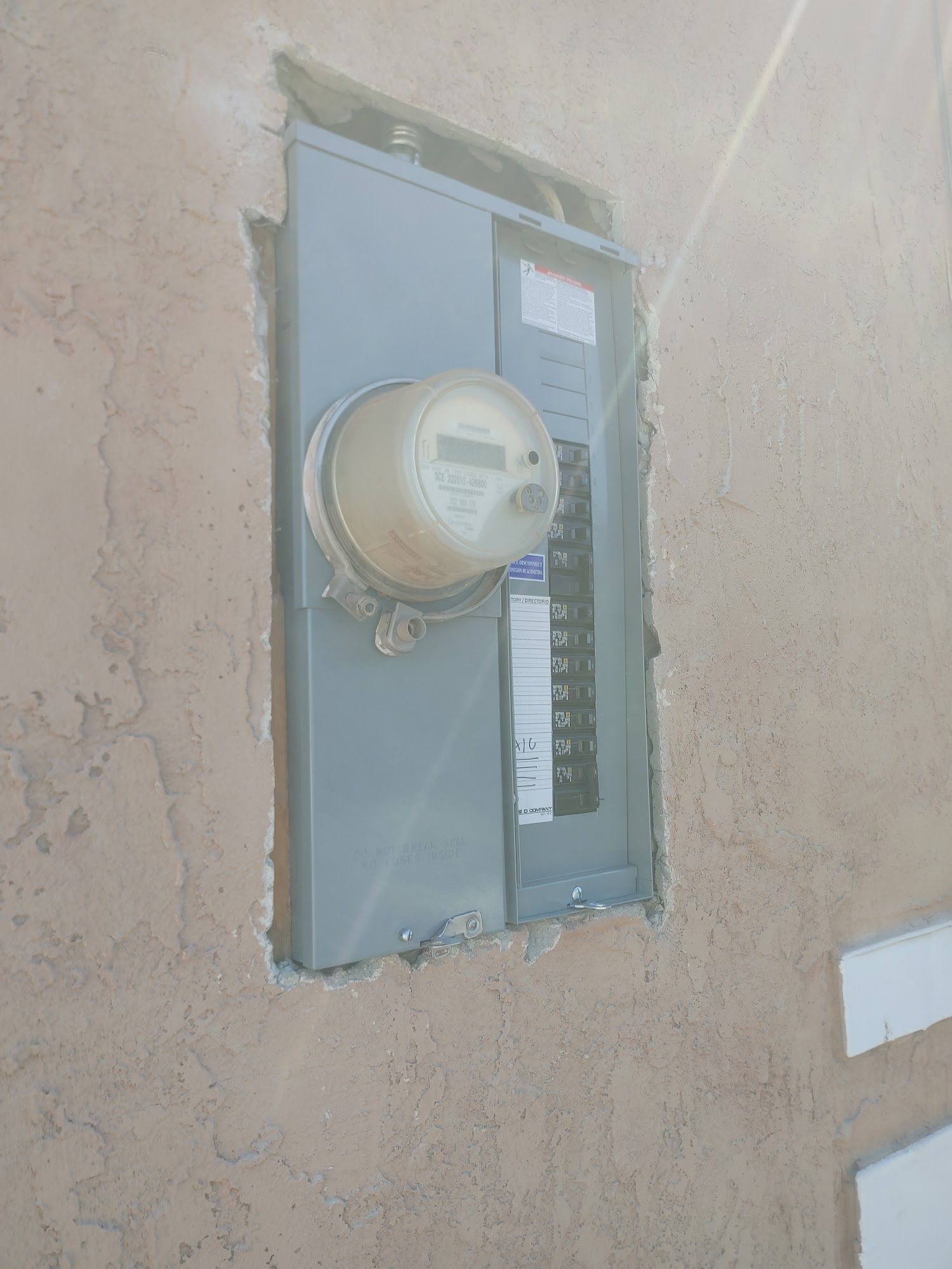 Electrical panel and meter recessed in a stucco wall. Gray metal components, cream meter, tan stucco.