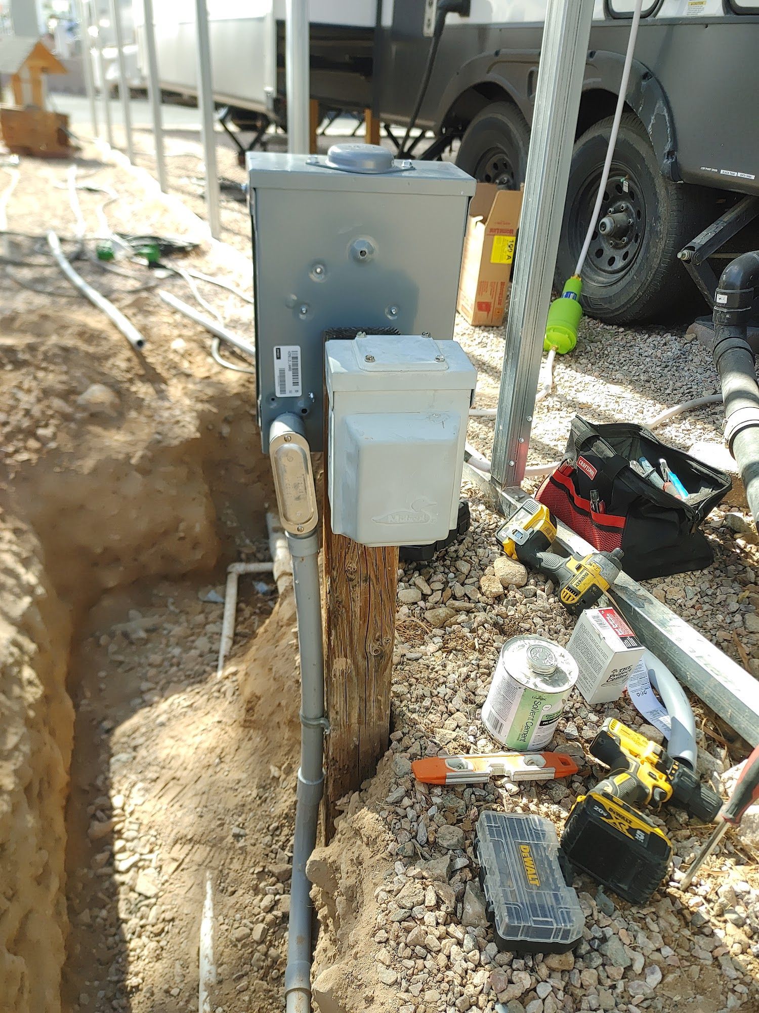 Electrical box mounted on a wooden post in an outdoor construction setting. Tools and conduit are visible nearby.
