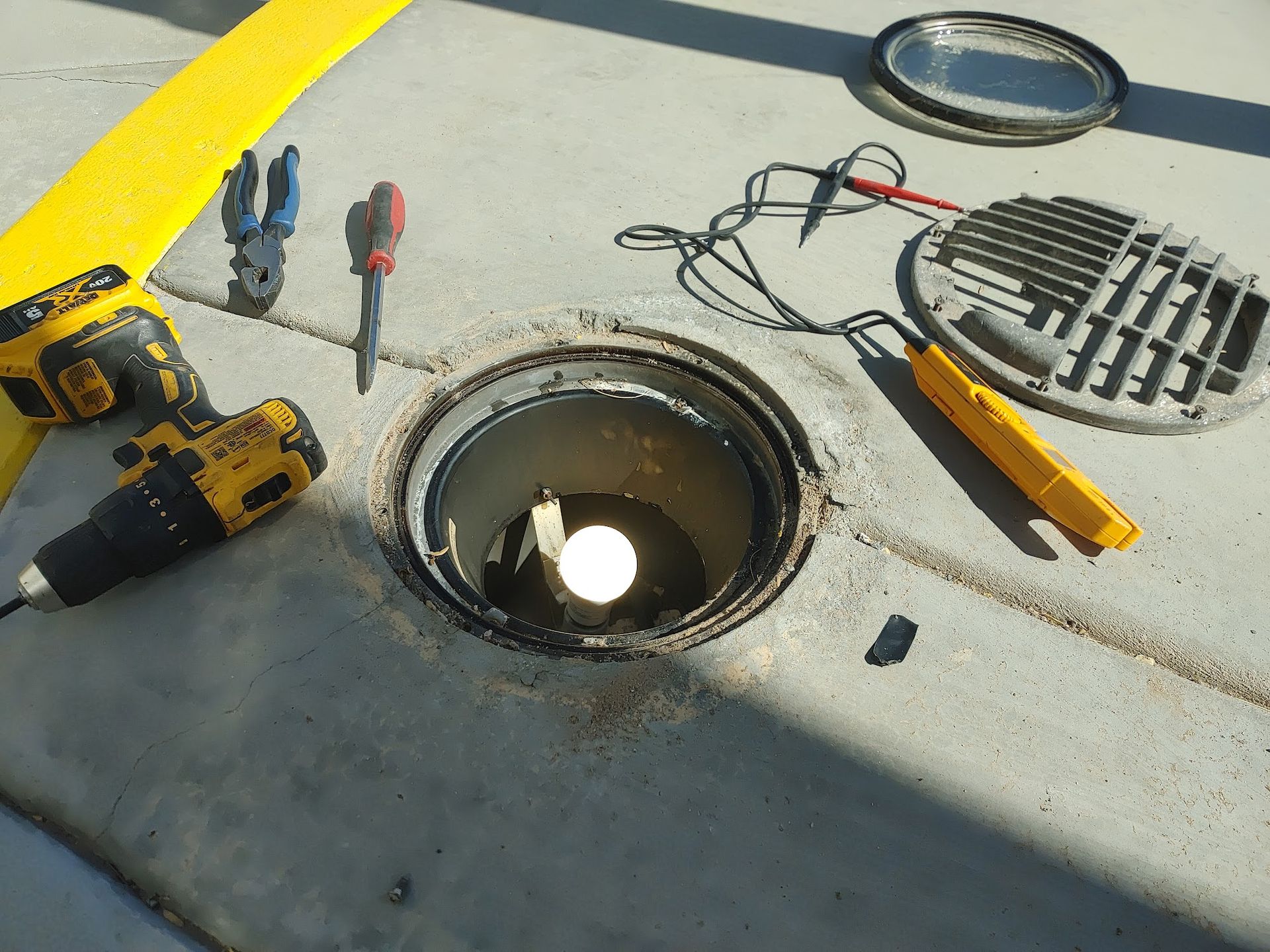 Tools and open access port on concrete surface, with a light visible inside.