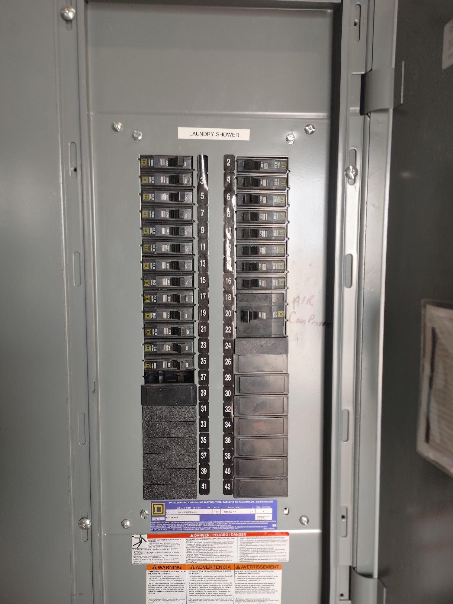 Electrical panel with rows of black circuit breakers. Metal door open, indoors.