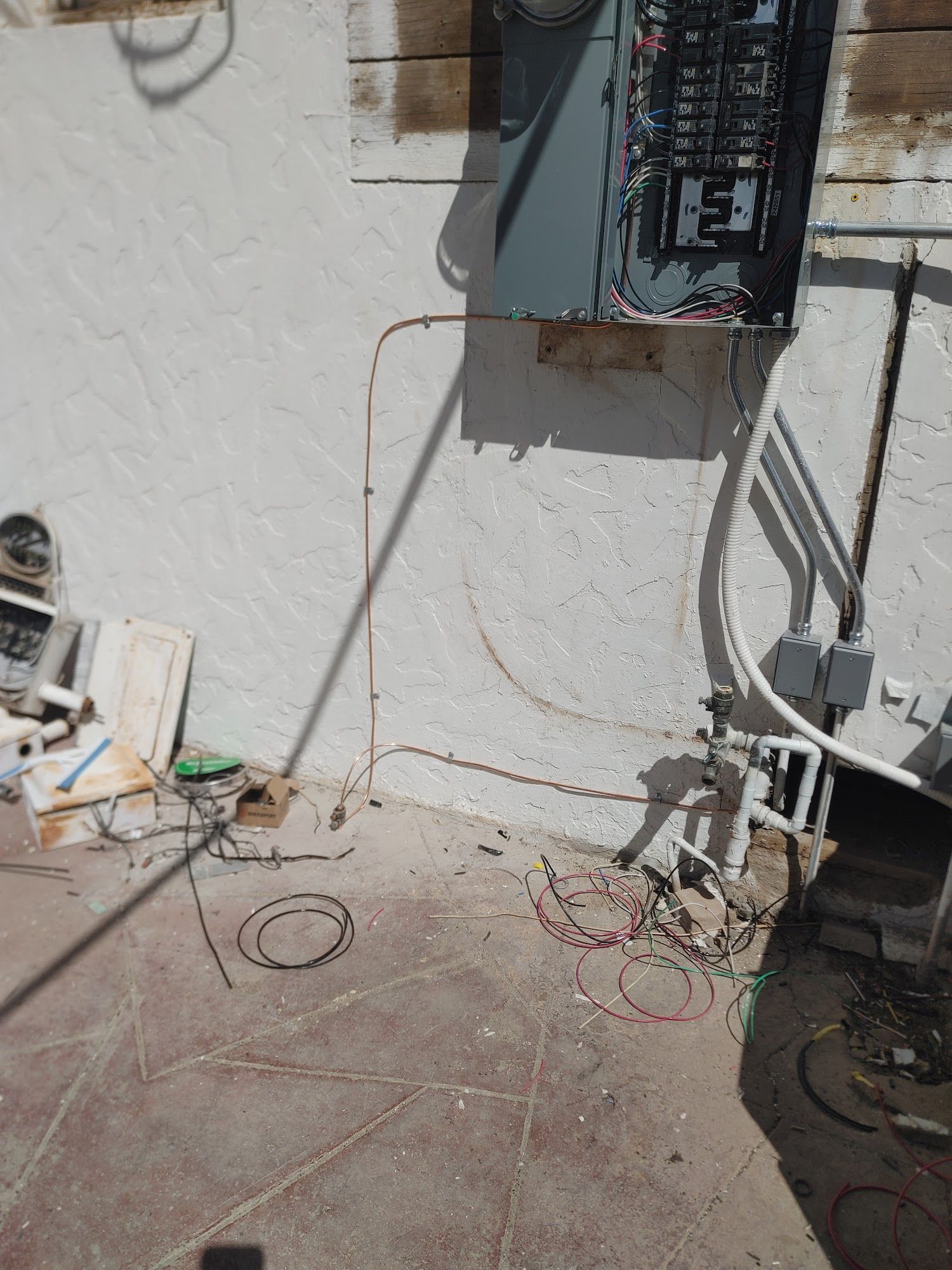 Electrical panel mounted on a stucco wall with exposed wiring and conduit on a concrete patio.