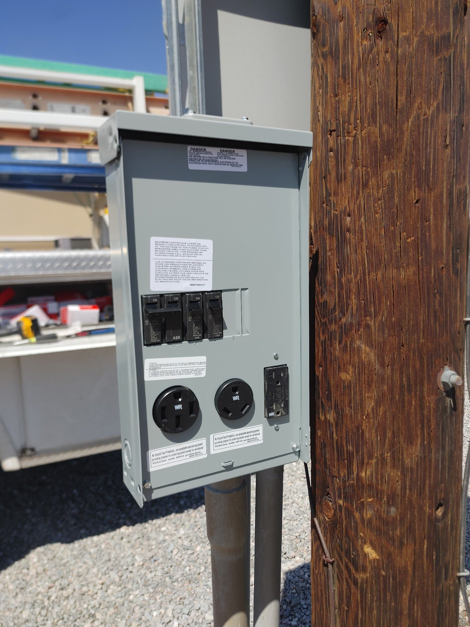 Gray electrical box with multiple outlets and switches mounted on a wooden post.
