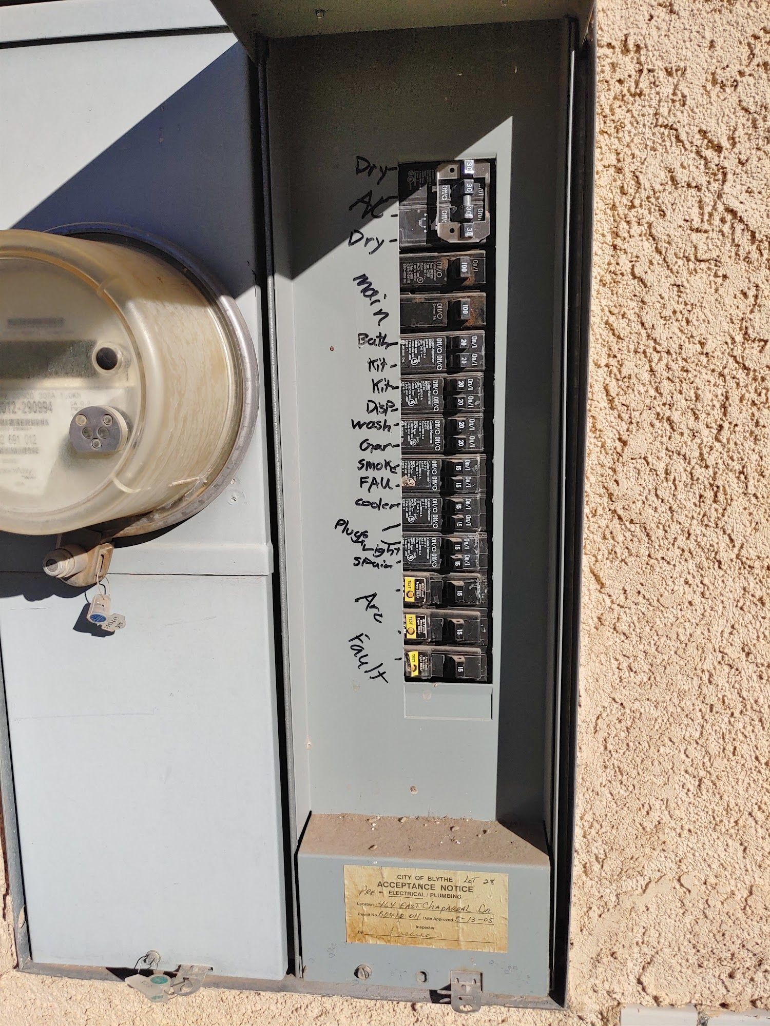 Electric panel with labeled circuit breakers. Grey metal box attached to stucco wall.