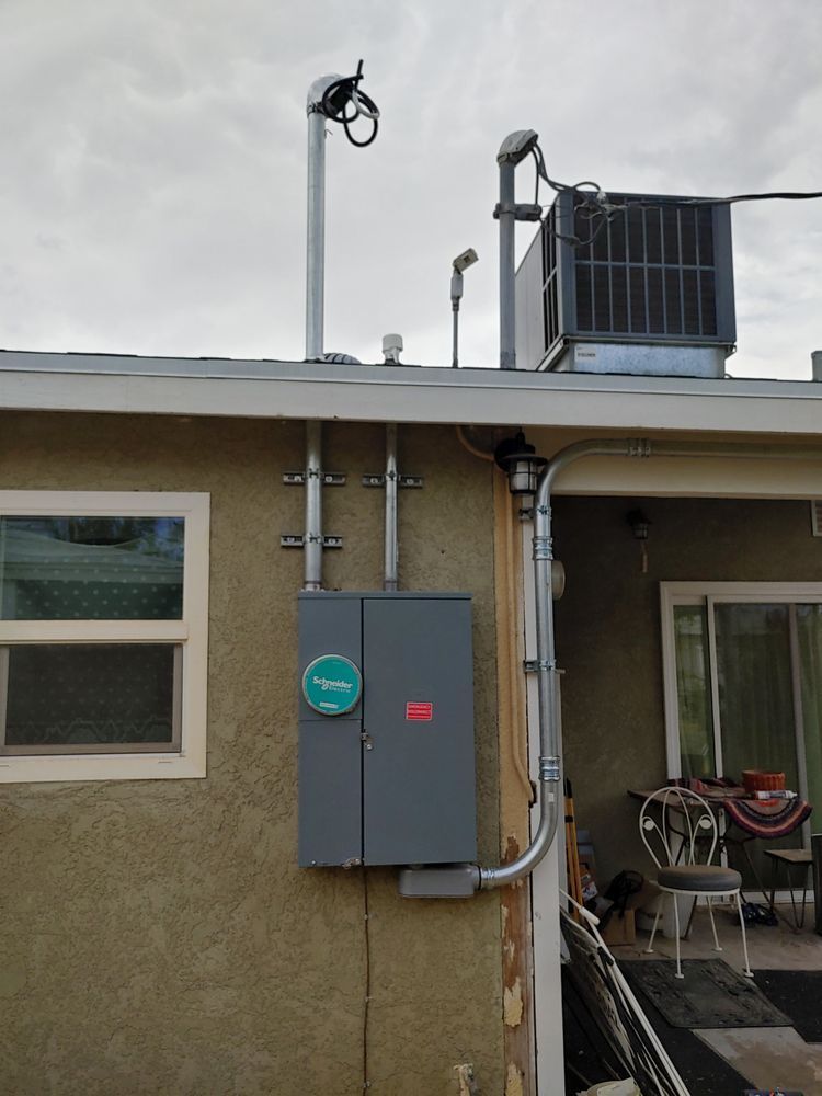 Gray electrical panel on a beige wall with metal conduit. A rooftop air conditioning unit is in the background.