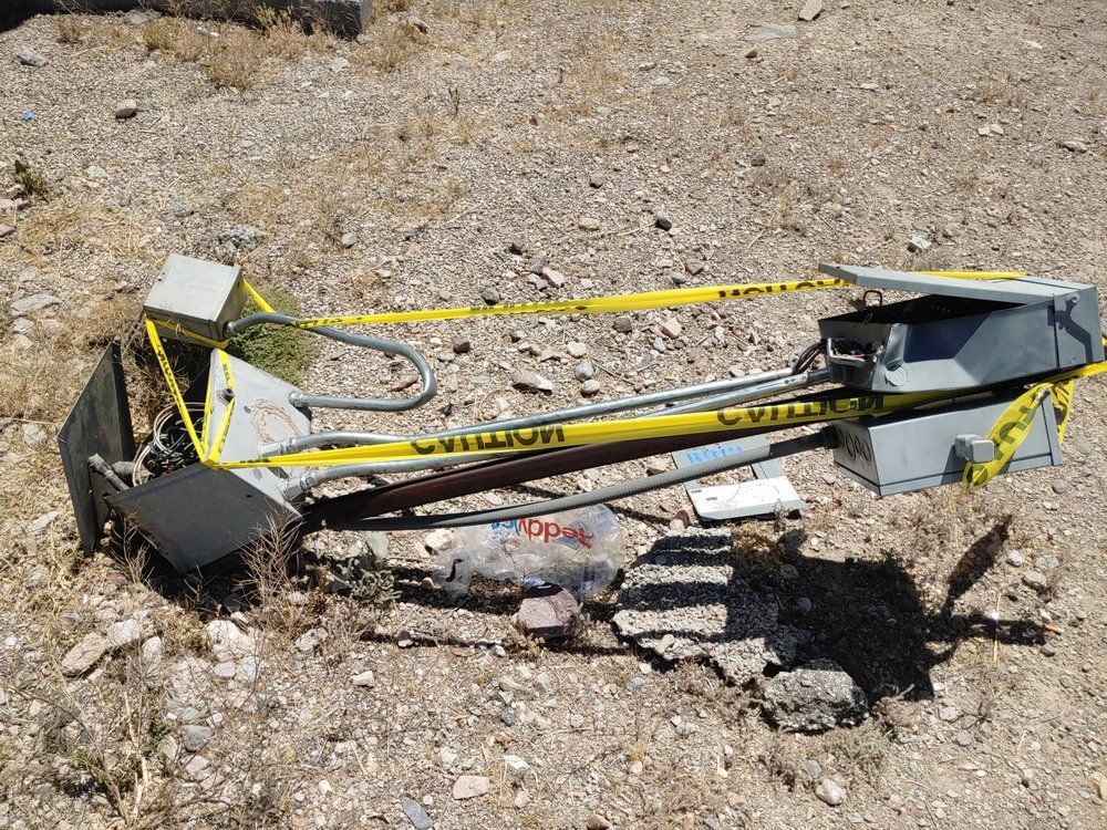 Fallen metal street light on ground, yellow caution tape, dirt and rocks, outdoors.
