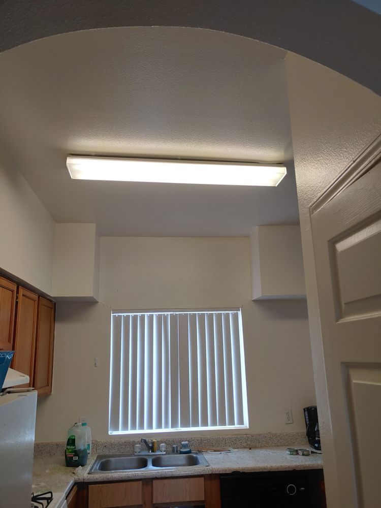 Kitchen with cabinets, sink, window with blinds, and fluorescent overhead lighting.