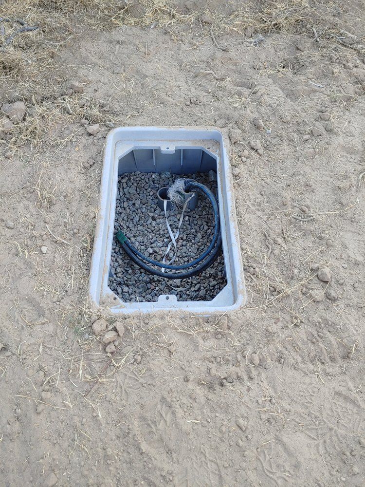 Open utility box in dirt, containing cables and gravel.