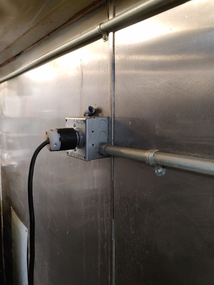 Metal wall with electrical outlet box and conduit. Black power cord plugged in.