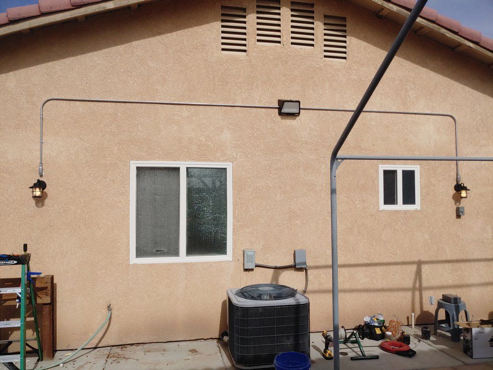 Tan stucco exterior with two windows, outdoor lighting, and an air conditioner unit.