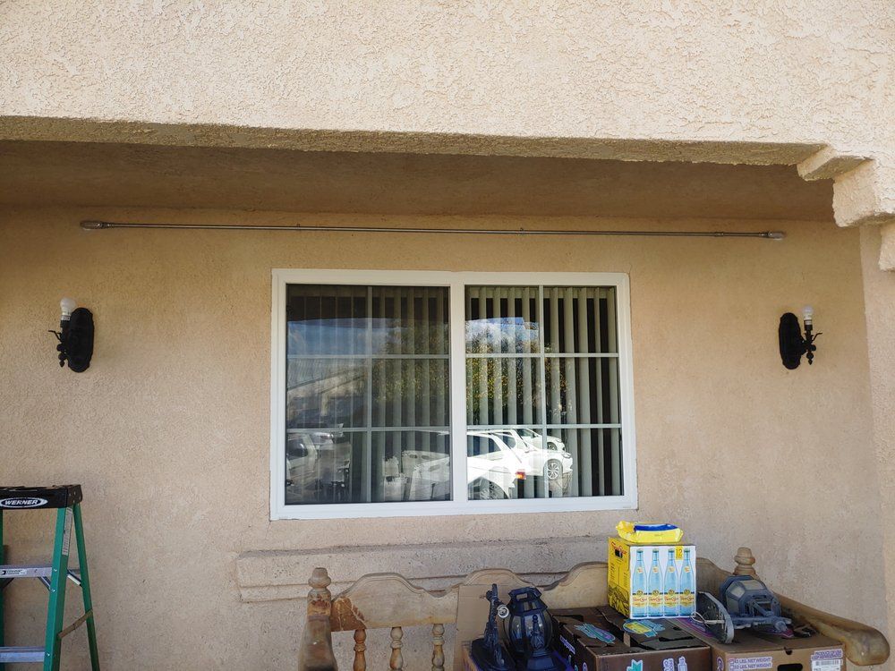 Exterior view of a window with vertical blinds, flanked by sconces on a stucco wall.