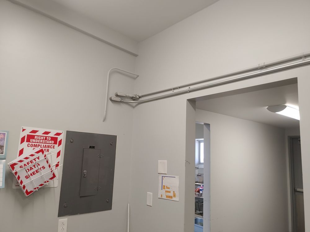 Electrical panel and conduit on a wall with safety signs and doorway.