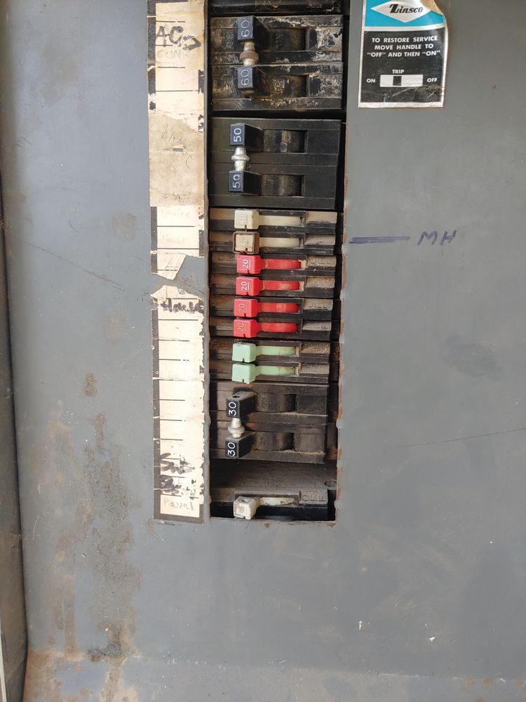 Electrical circuit breaker panel with various colored switches in a gray metal box.