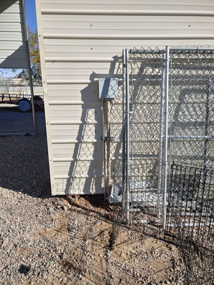 Metal shed with electrical box and chain-link fence on gravel ground.