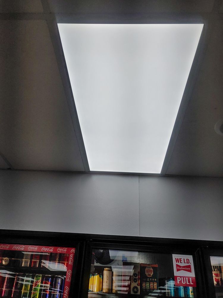 Bright fluorescent light fixture on a white ceiling above a cooler filled with products.