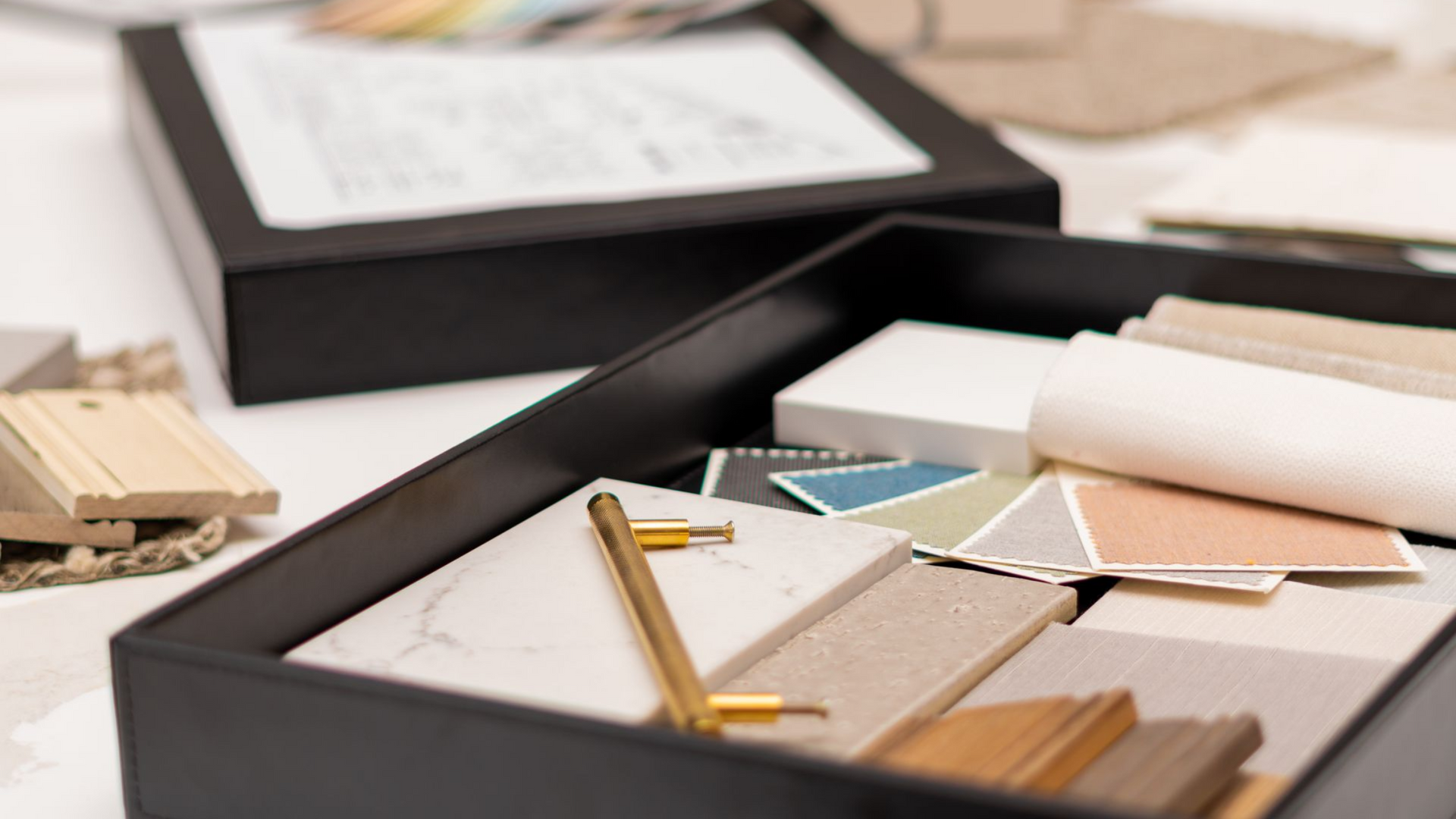 A black box with interior design samples: tiles, handles, paint swatches, and a schematic document.
