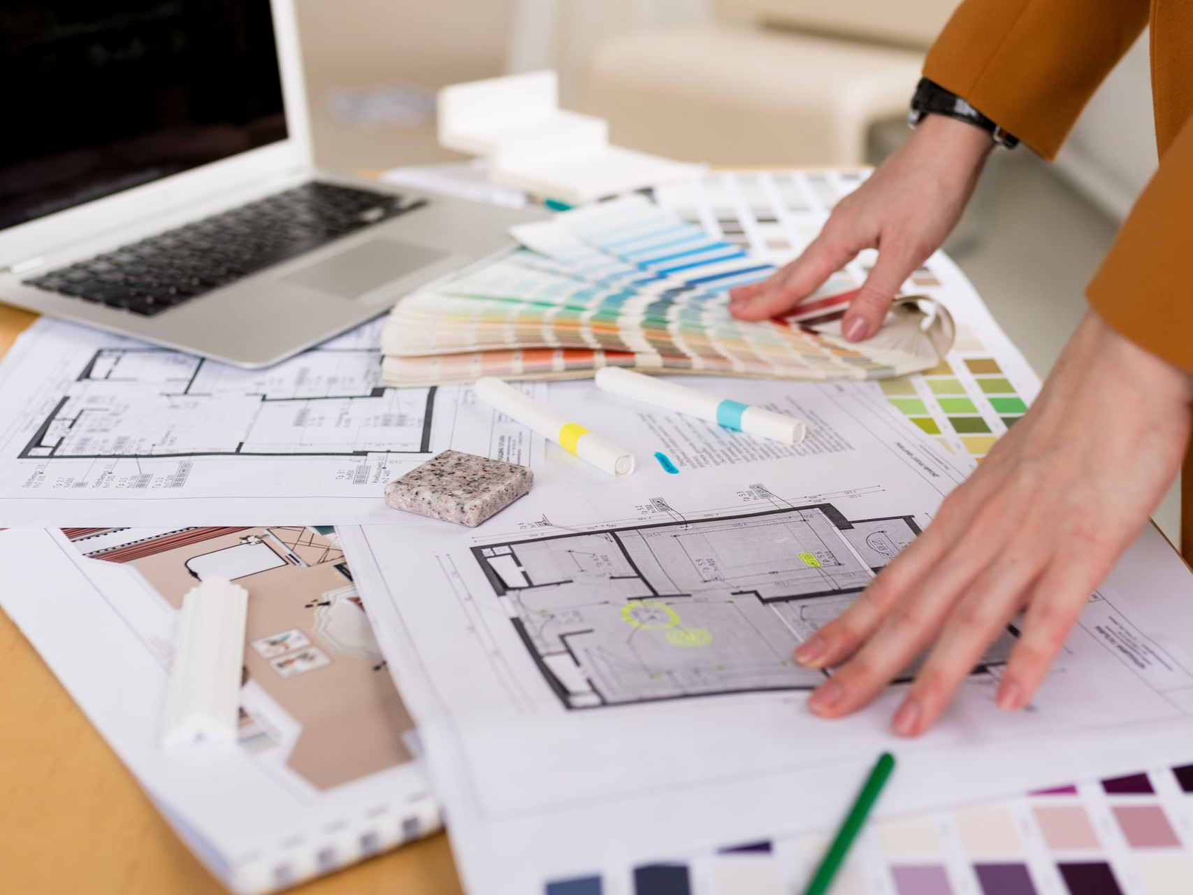A person with hands on blueprints, choosing paint colors, with laptop and design samples.