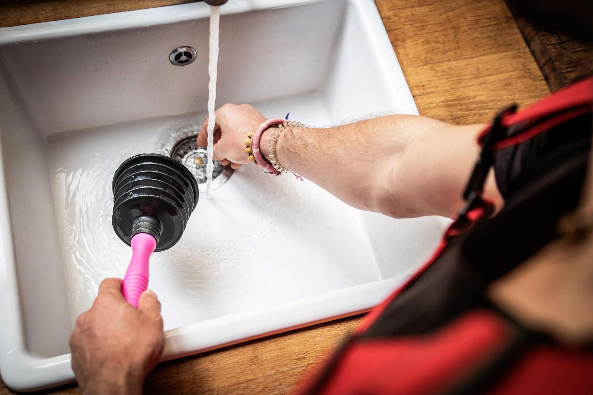 Man holding plunger working on sink — Fort Smith, AR — Benefit Plumbing