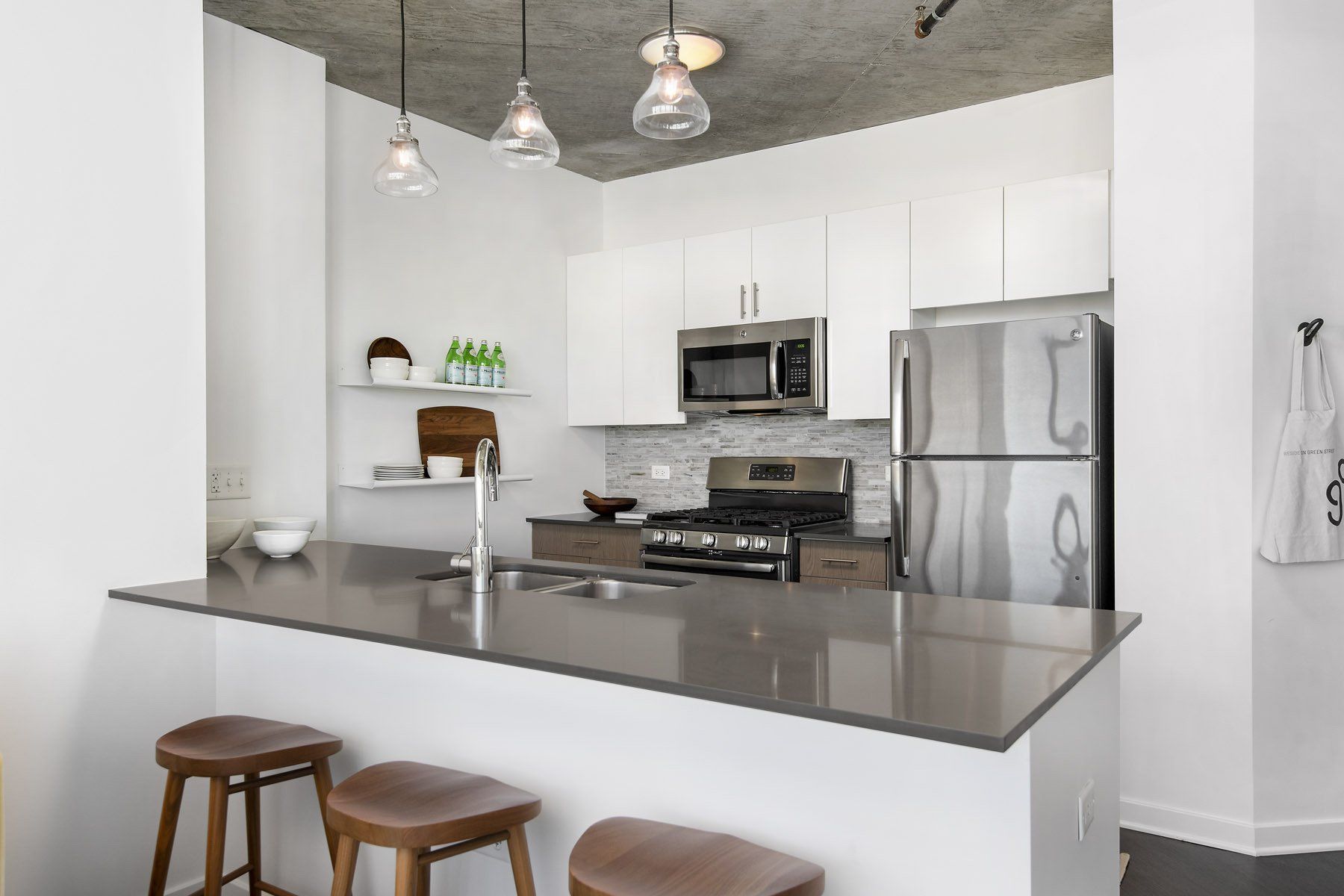 A kitchen with white cabinets and stools and a stainless steel refrigerator  at Reside on Green Street.