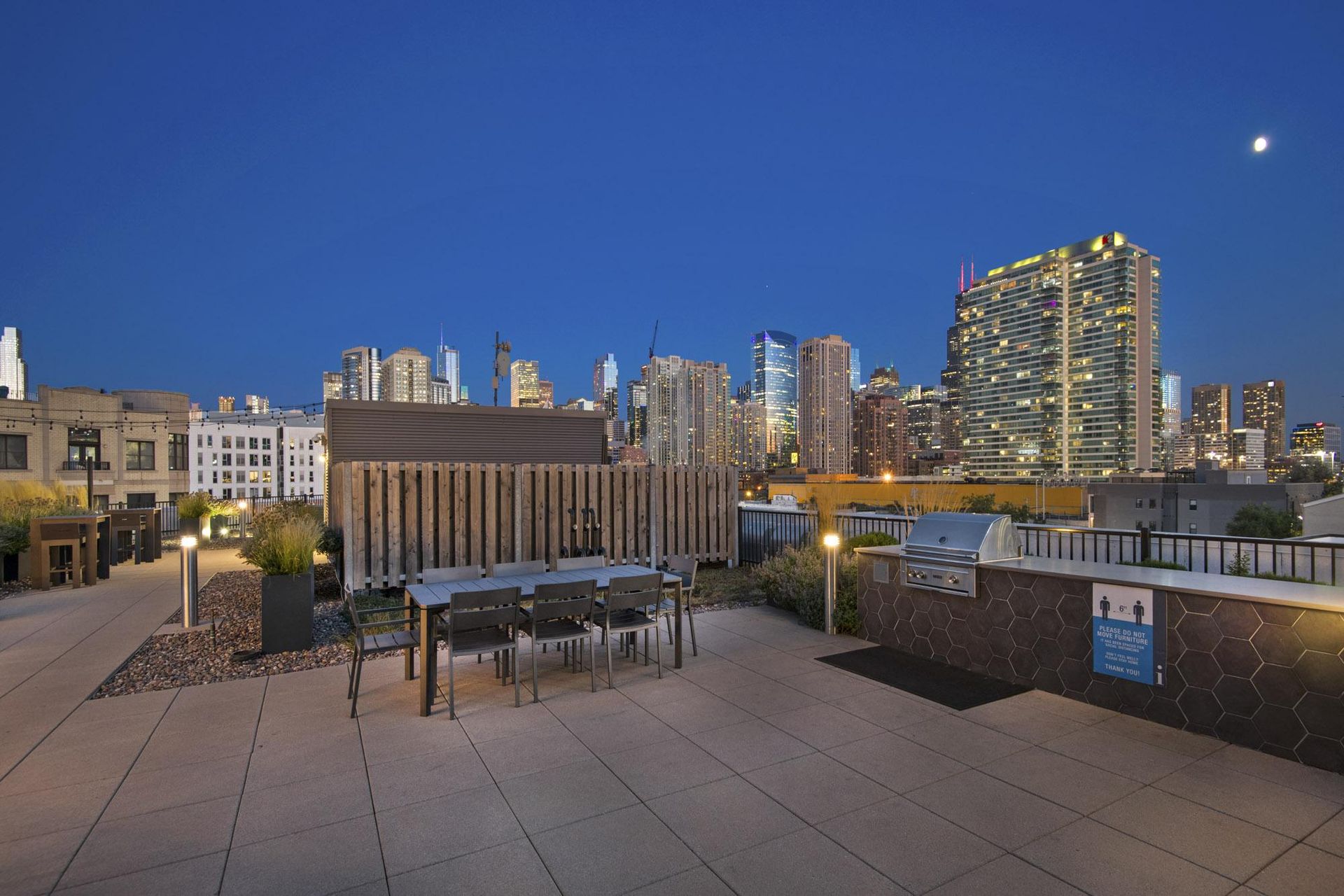 a rooftop terrace with a dining table and a view of the city at night