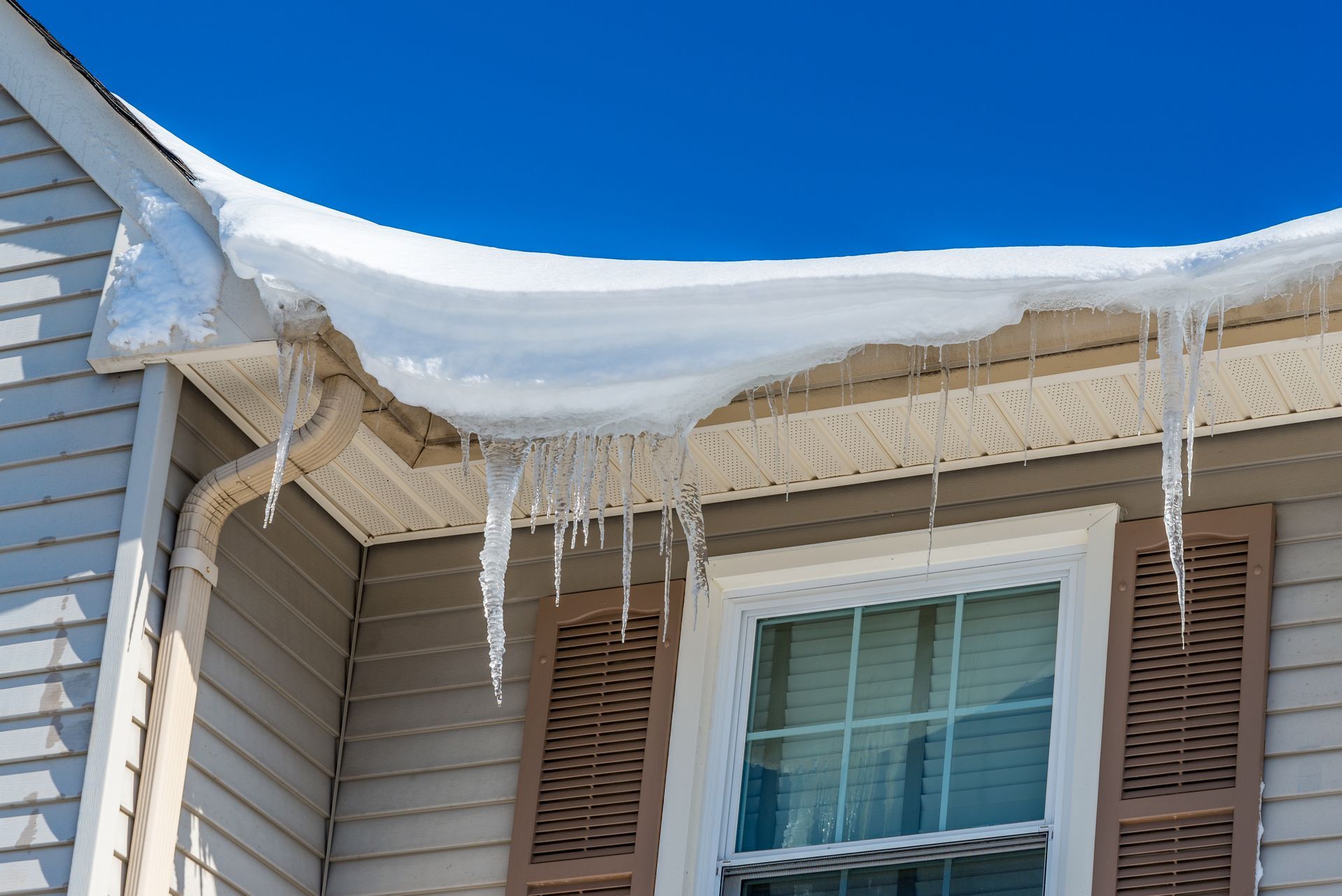 Snow hanging over a roof edge with long icicles forming above a residential window Snow hanging over a roof edge with long icicles forming above a residential window