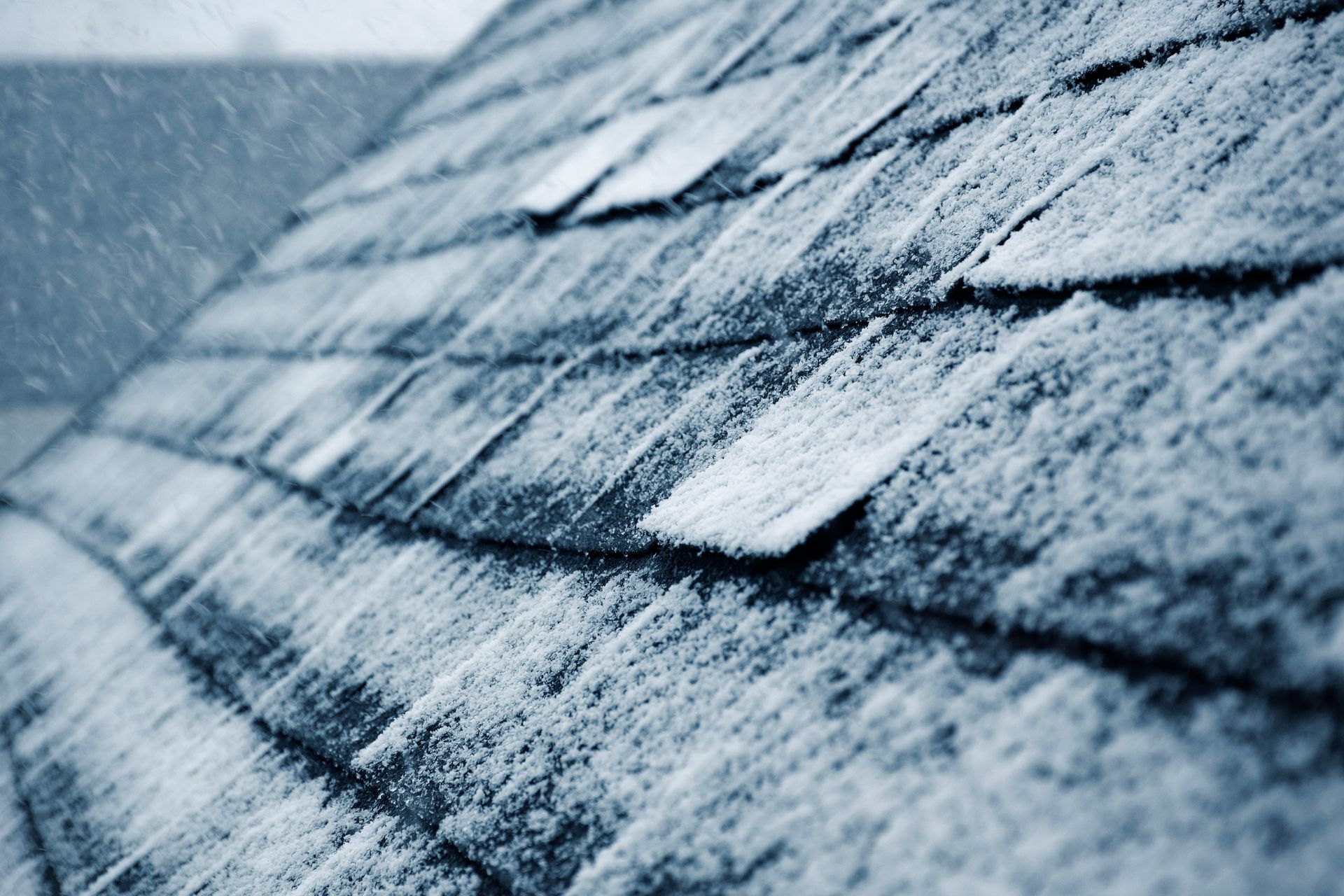 Snow-covered roof shingles during a winter storm showing icy buildup across a residential rooftop