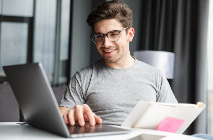 A man wearing glasses is sitting at a desk using a laptop computer.
