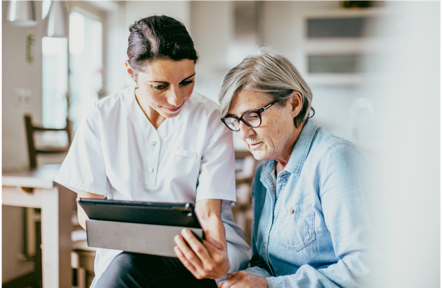 A nurse is helping an elderly woman use a tablet computer.