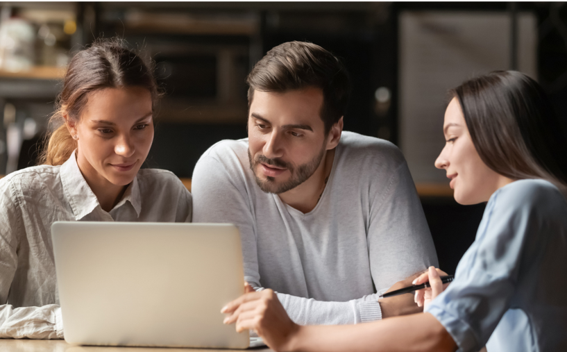 A group of people are sitting at a table looking at a laptop computer.