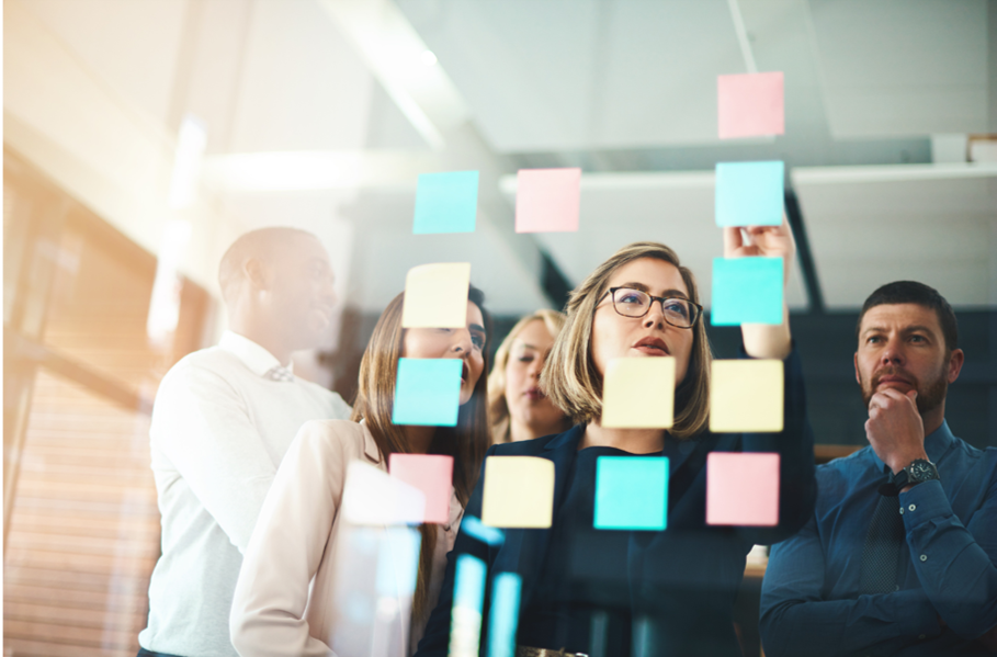 A group of people are looking at sticky notes on a glass wall.
