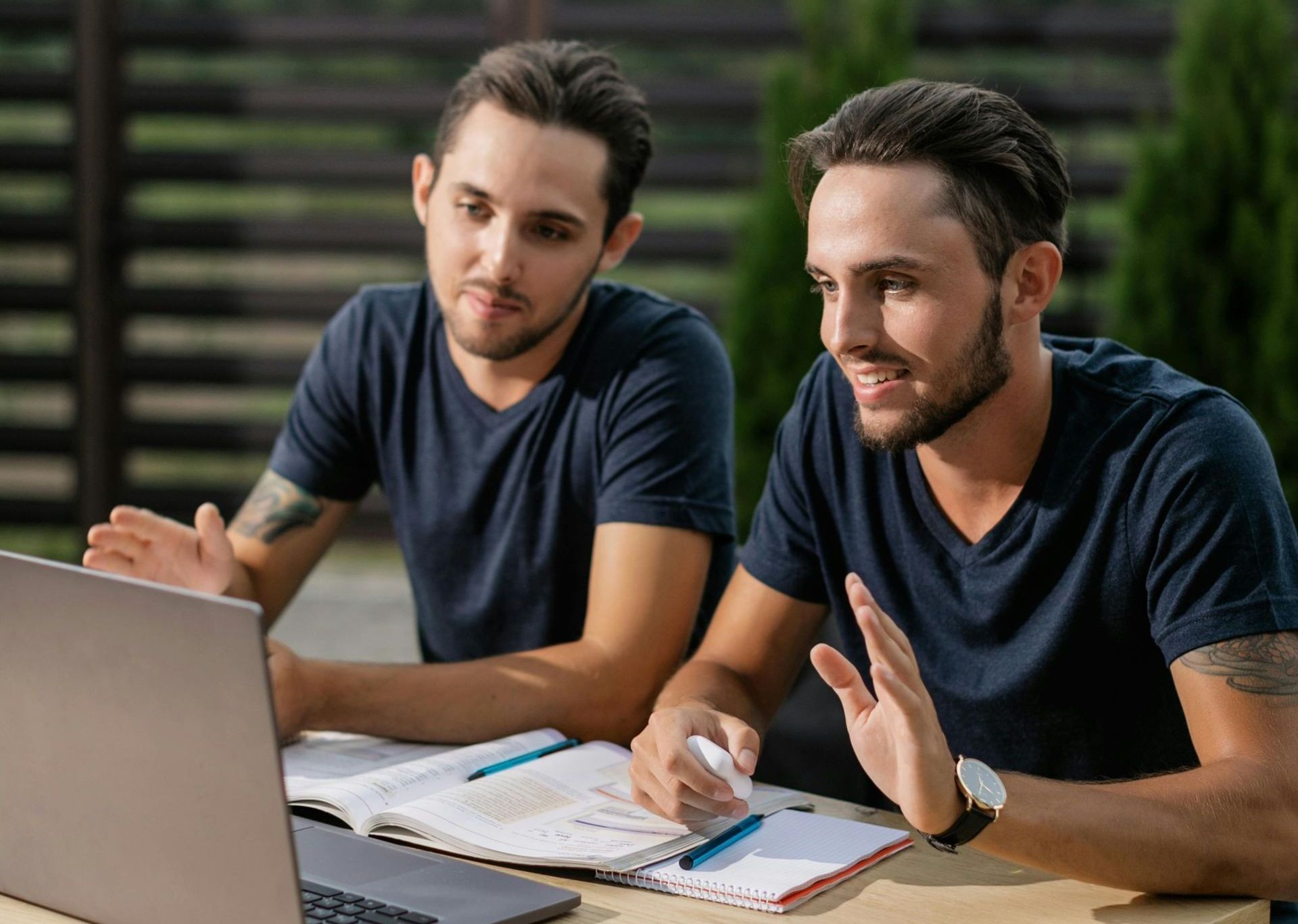 Two men are sitting at a table looking at a laptop computer.