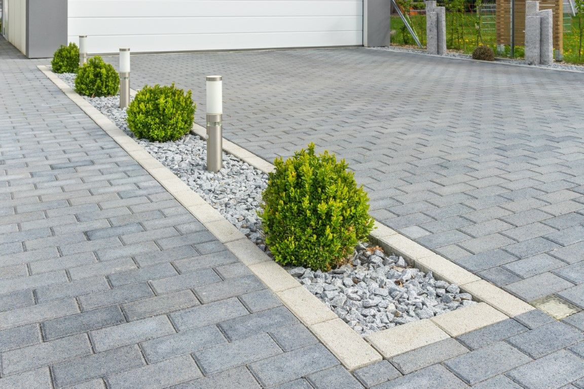 A brick driveway with a row of bushes and gravel.