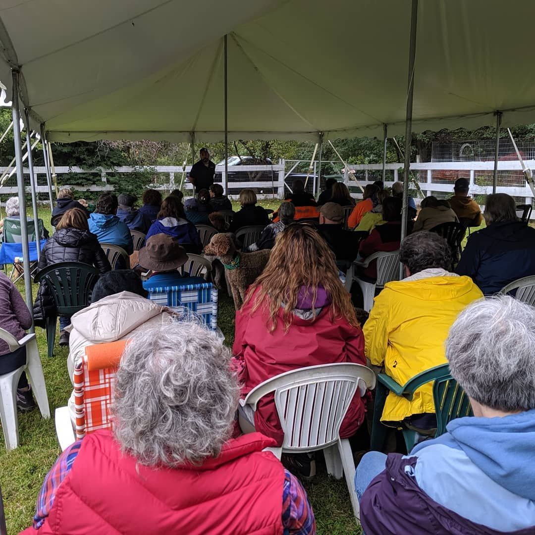 A group of people sitting under a white tent listening to a speaker