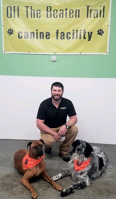 Man with two dogs in a canine facility, under a banner that reads “Off The Beaten Trail”.