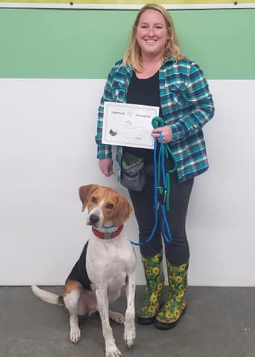 A women in a blue flannel standing with her dog and a training Certificate
