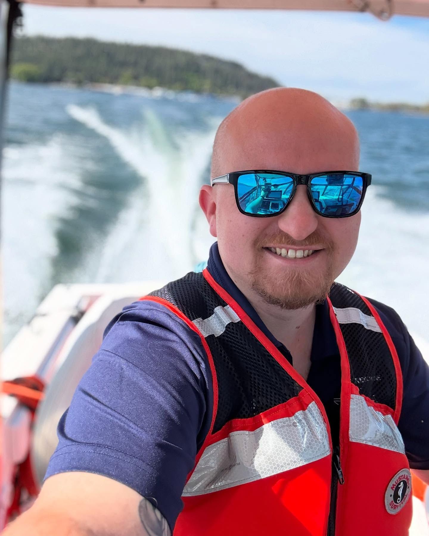 Austin Munda with two  men in blue shirts and shorts walk on a dock, carrying orange bags, near water and a tall building.