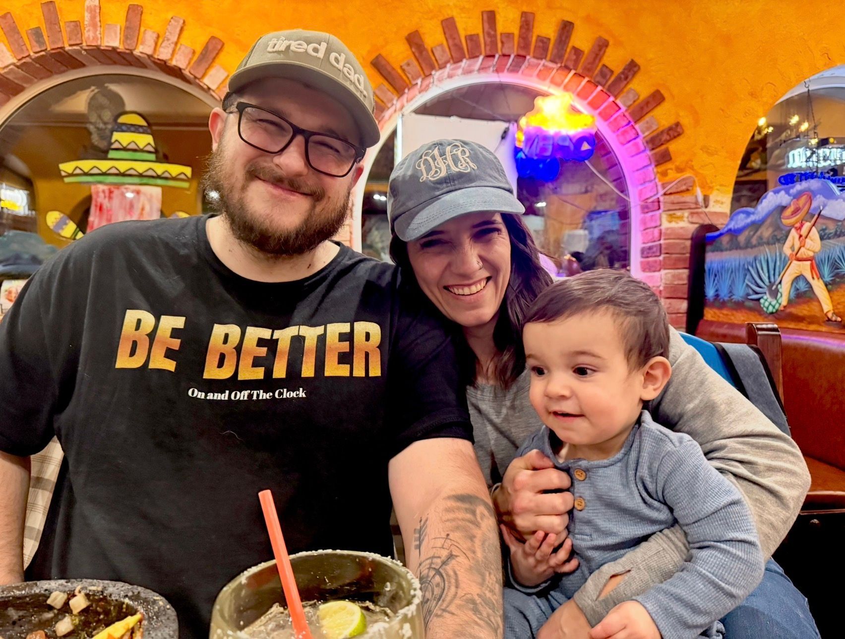 Joshua Miller smiling at a restaurant.With his partner and baby son.