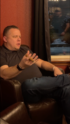 Brian Horan seated in leather chair, holding cigar, talking, interior setting.